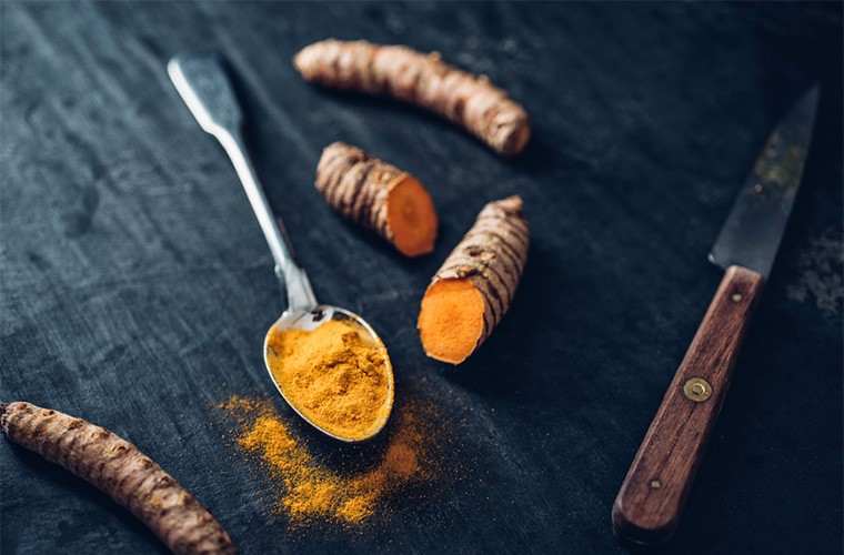 A tablespoon of turmeric situated next to fresh turmeric.