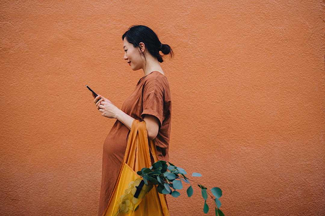 Pregnant woman walking with groceries looking at phone