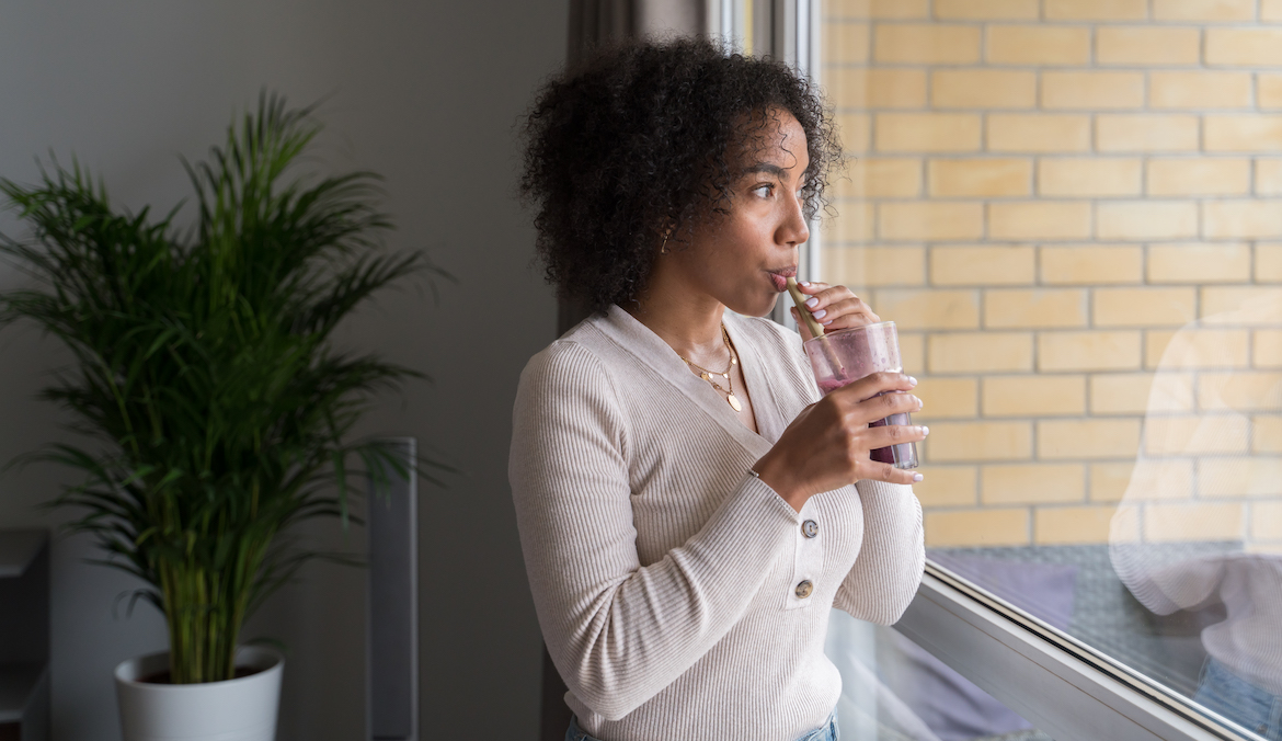 A woman drinks a beverage through a straw while looking out a window.