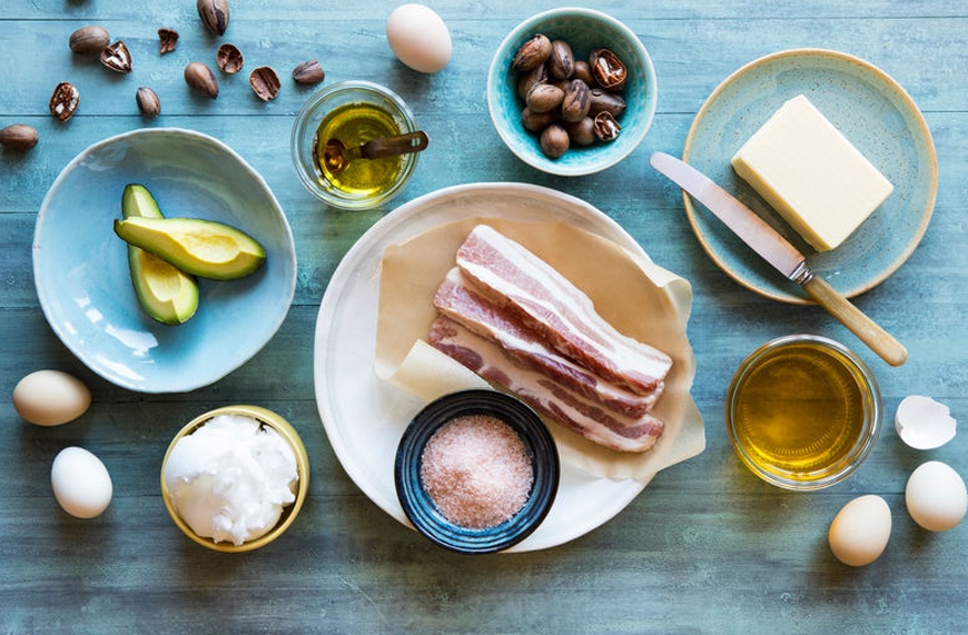 Table with several plates of different keto foods, including bacon, avocado, and oils.