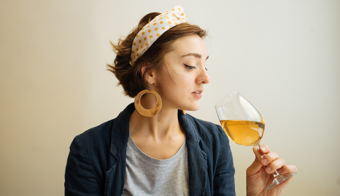 A woman holds a wine glass up to her nose and examines the wine inside it.