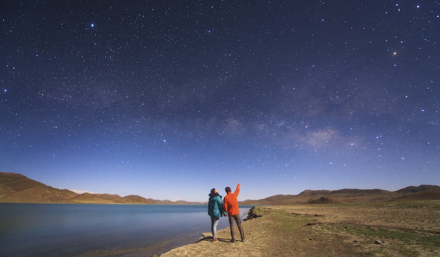 A couple enjoys a romantic moment under the Milky Way on a moonlit night in Tibet, China.