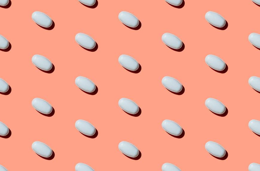 name brand vs generic drugs pills lined up on salmon-colored backgrond