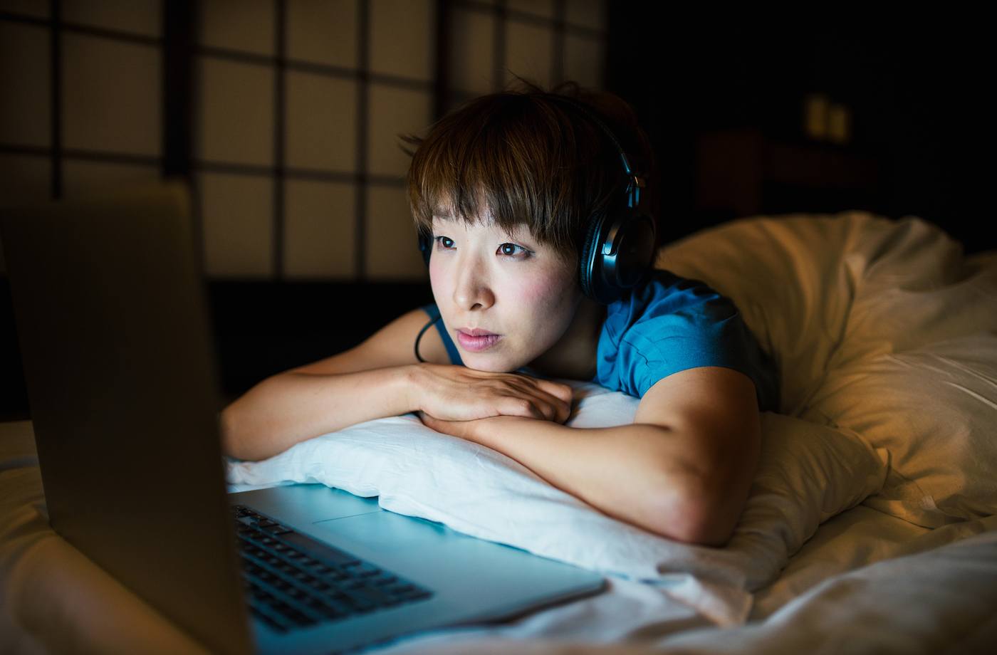 woman in bed with headphones watching tv on laptop poor impulse control