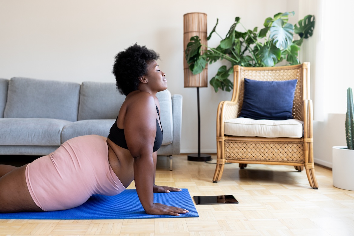 Person wearing black sports bra and pink shorts doing a dynamic stretch in living room