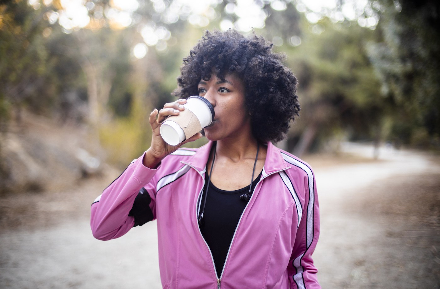 coffee before workout woman in running jacket drinking travel mug of coffee