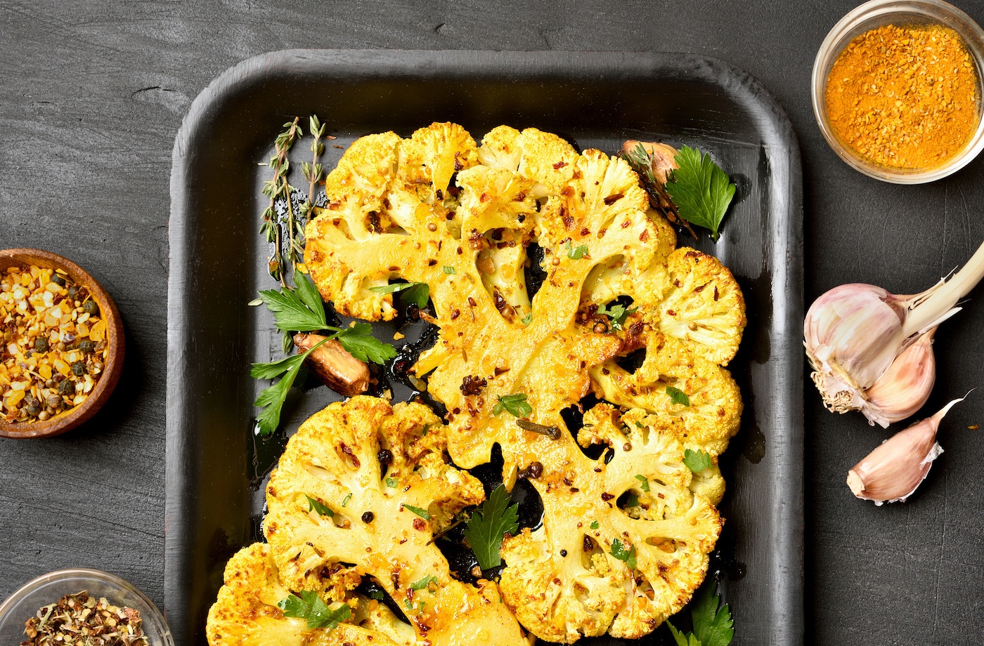 Cooked cauliflower, a food high in sulfur, sits on a baking sheet surrounded by spices and a sauce.