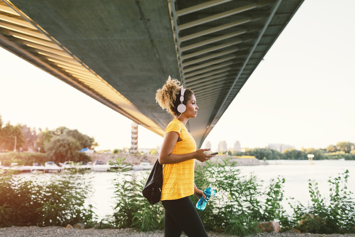 A woman with her headphones on walks underneath a bridge.