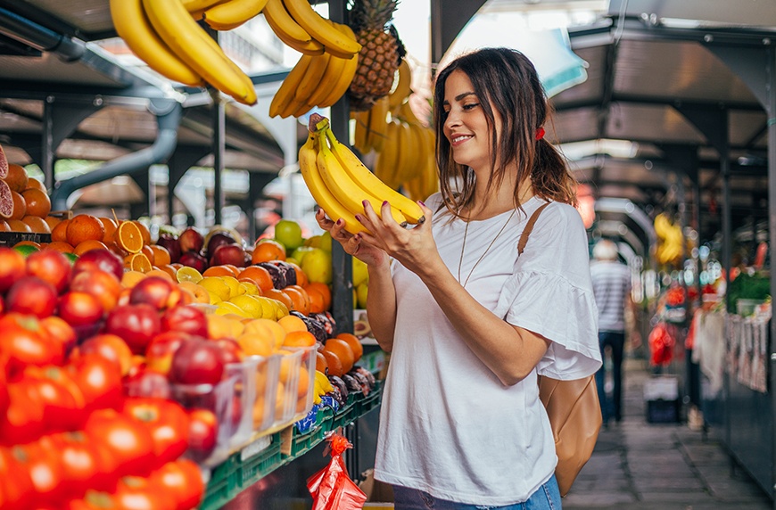 A woman holding a bunch of bananas at a fruit stand.