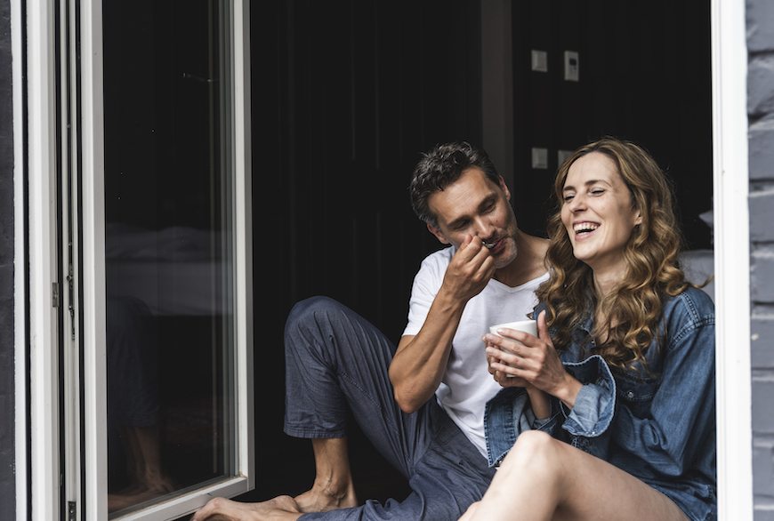 A couple shares an intimate moment—a man takes a spoon of his laughing partner's coffee using a spoon.