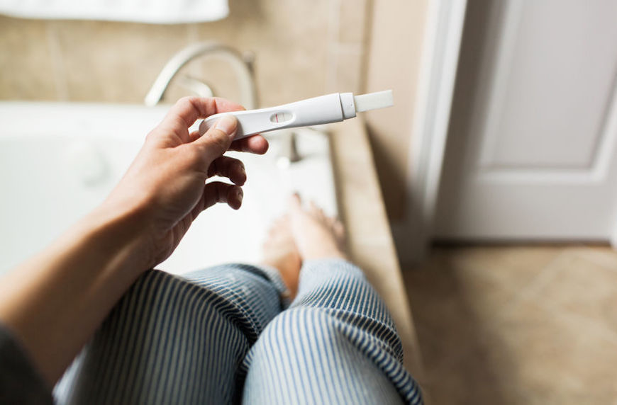 woman holding pregnancy test while sitting on bathtub