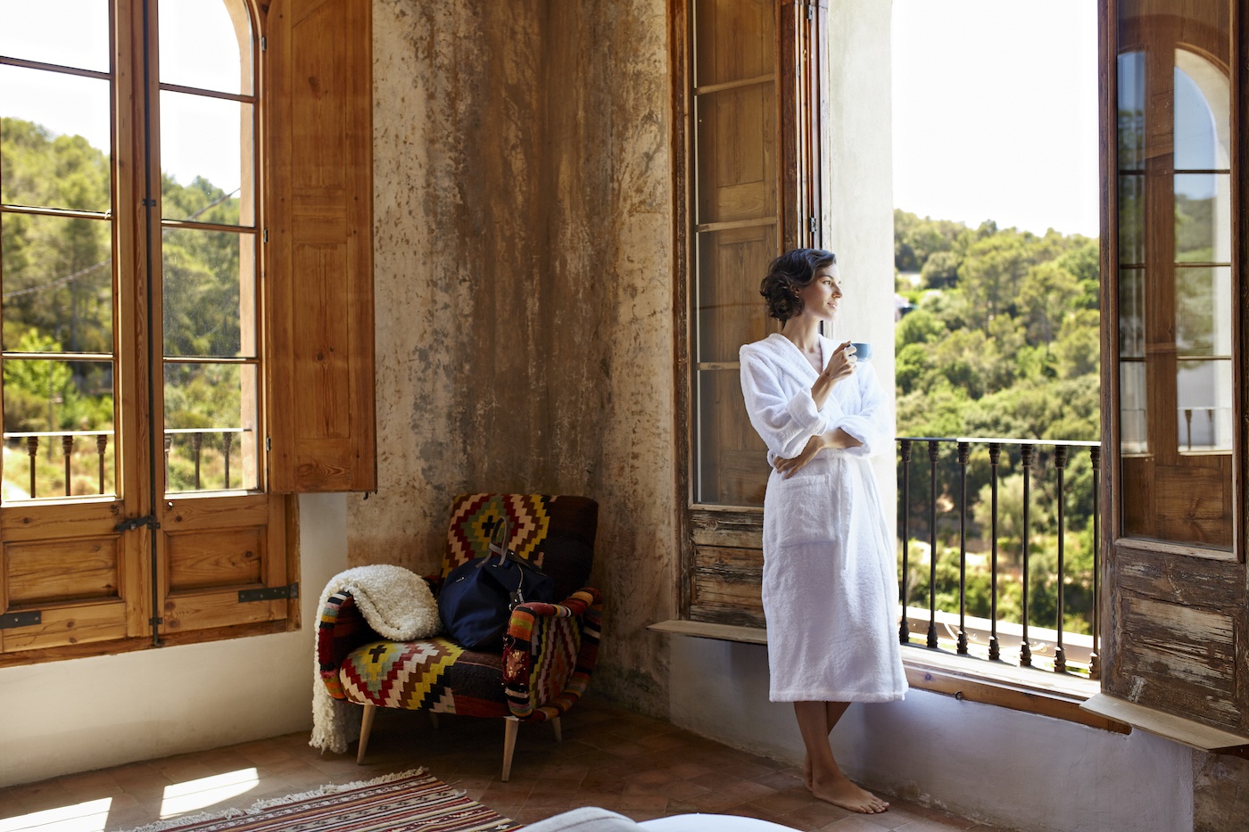 A woman in a bathrobe looking at the view outside a balcony.