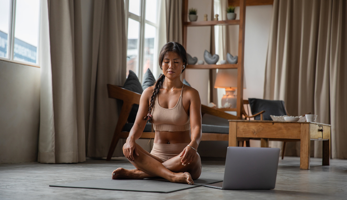 A woman sits cross-legged on a yoga mat while meditating.