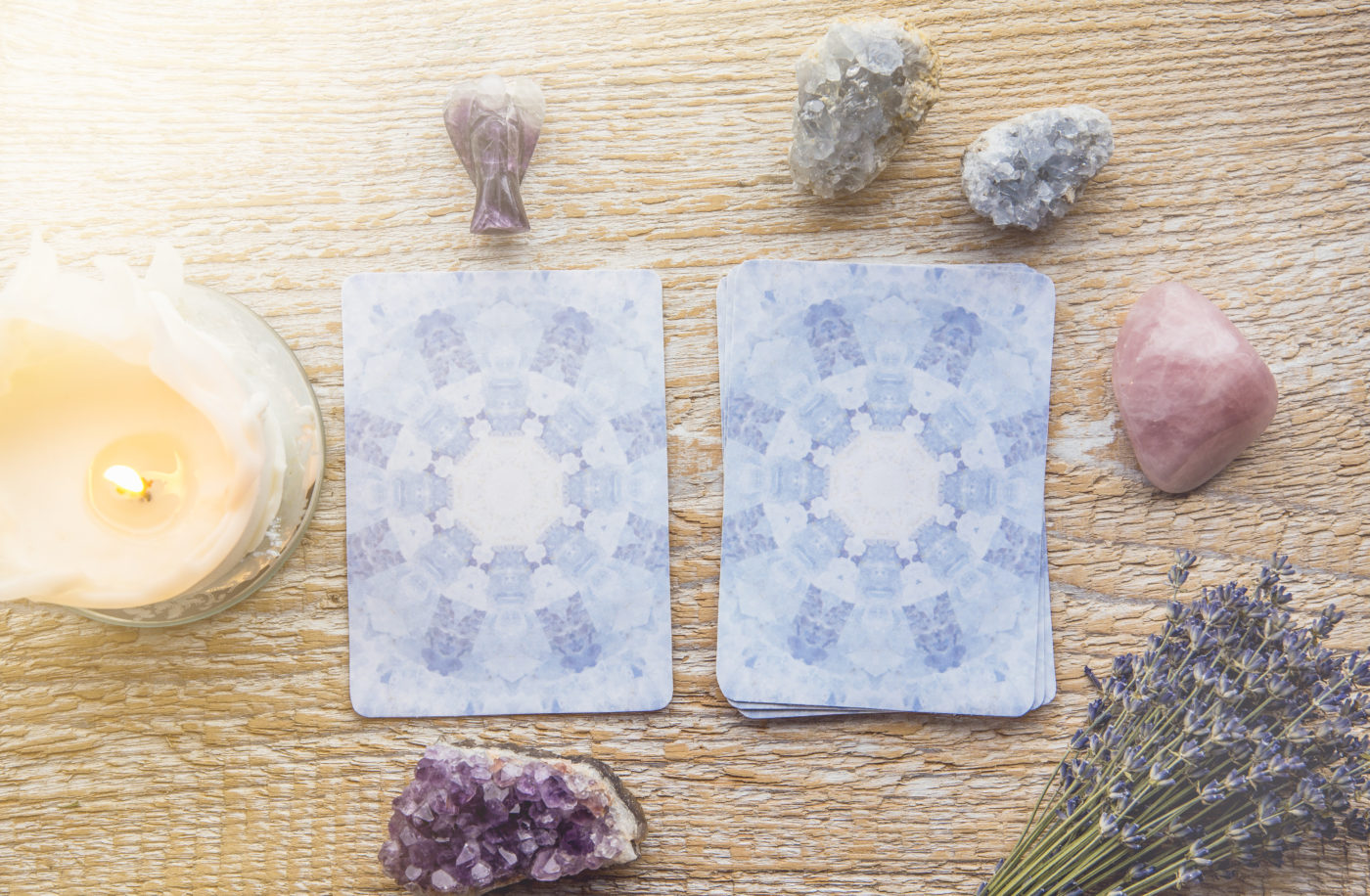 Two powder blue oracle cards are laid flat on a table next to a candle and some crystals and herbs.