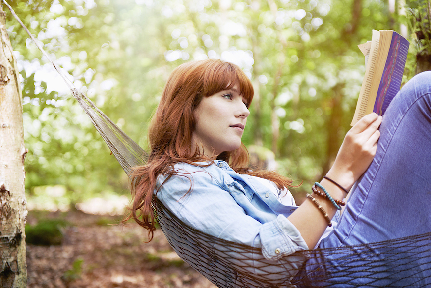 A woman in a hammock outside reading a book.