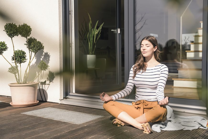 A woman sits on her porch and does yoga.