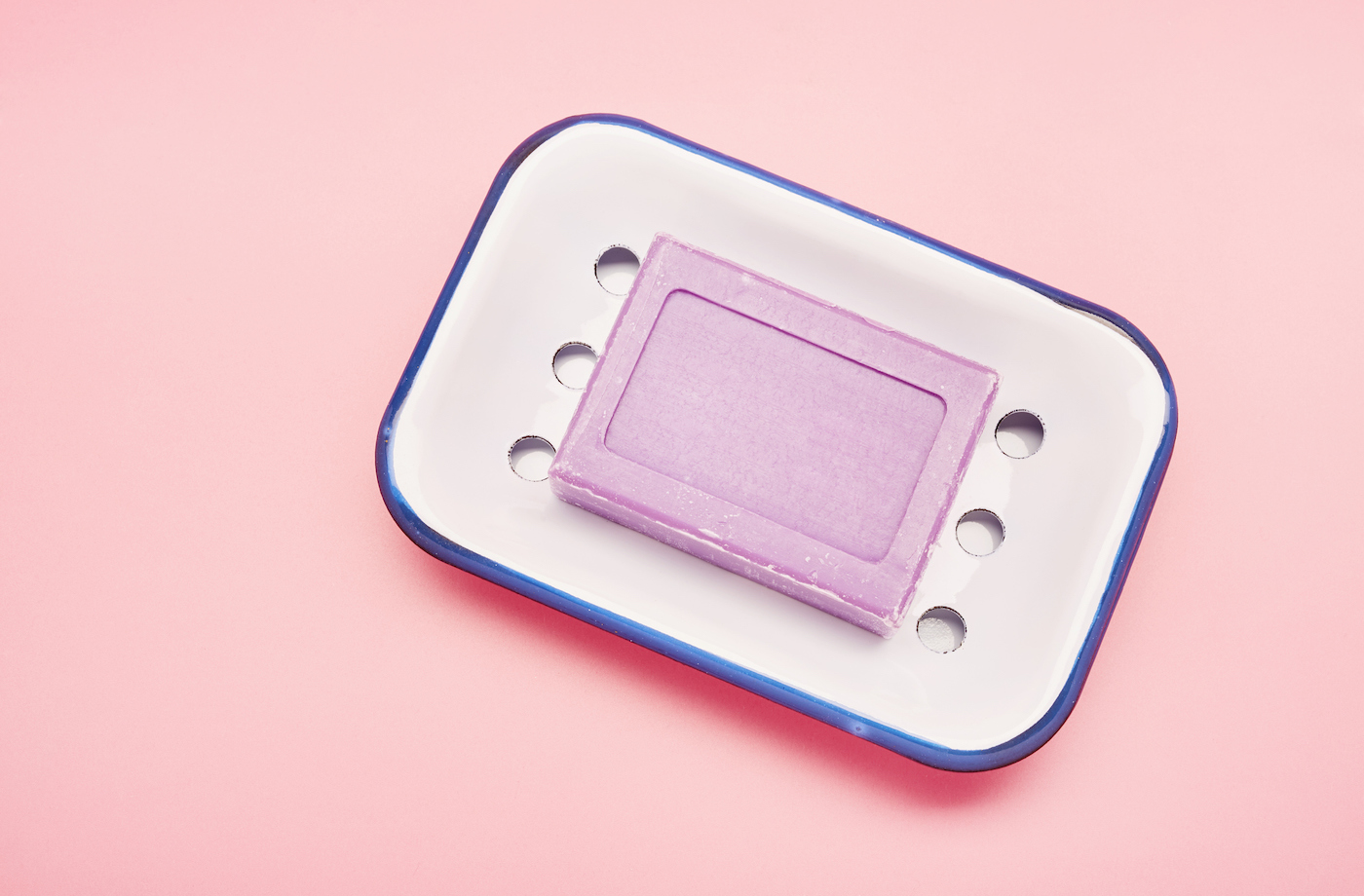 A pink bar soap on a white soap dish with drain holes.