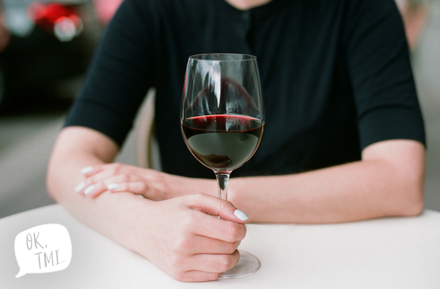 A woman clutches a half glass of red wine by its stem.
