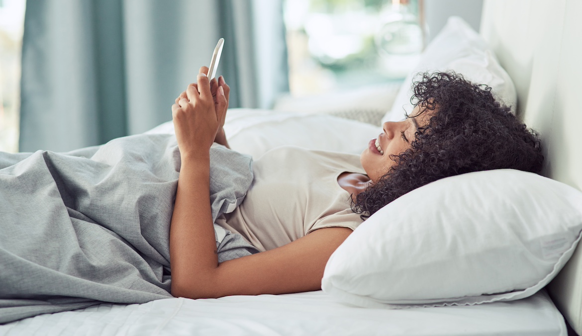 Woman texting in bed, symbolizing long distance sex