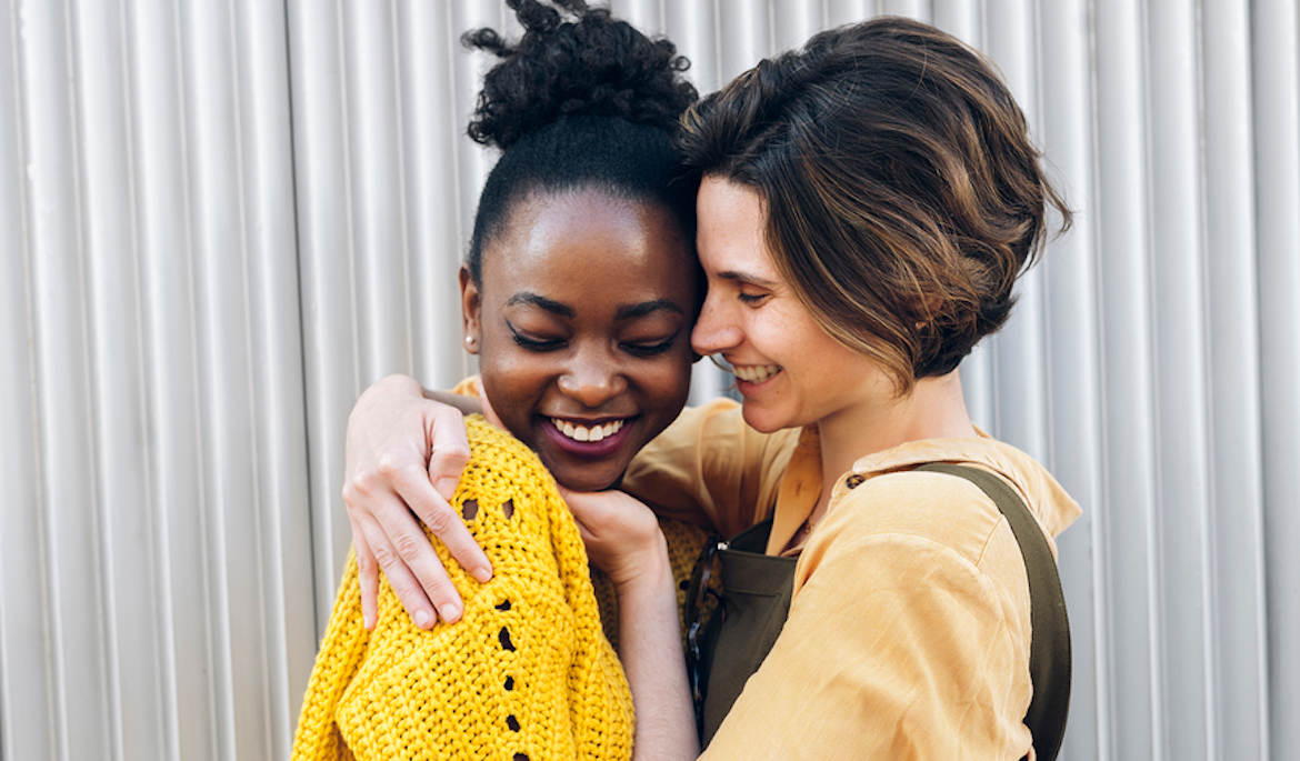 A lesbian multiracial couple smiles and embraces each other.
