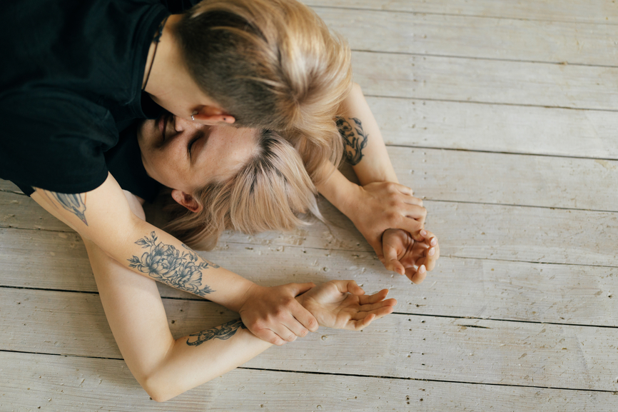 A woman pins her partner on the floor while holding her wrists over her head.