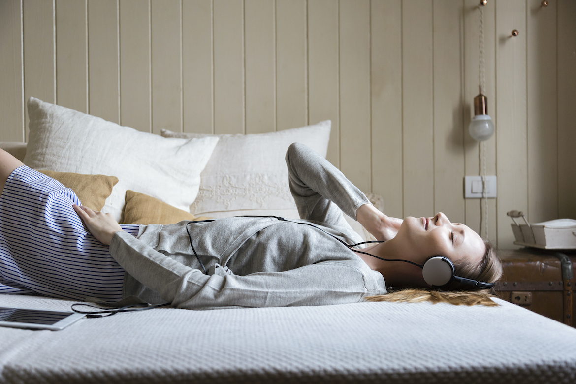 A woman lying in bed listens to sleep stories for adults with headphones.