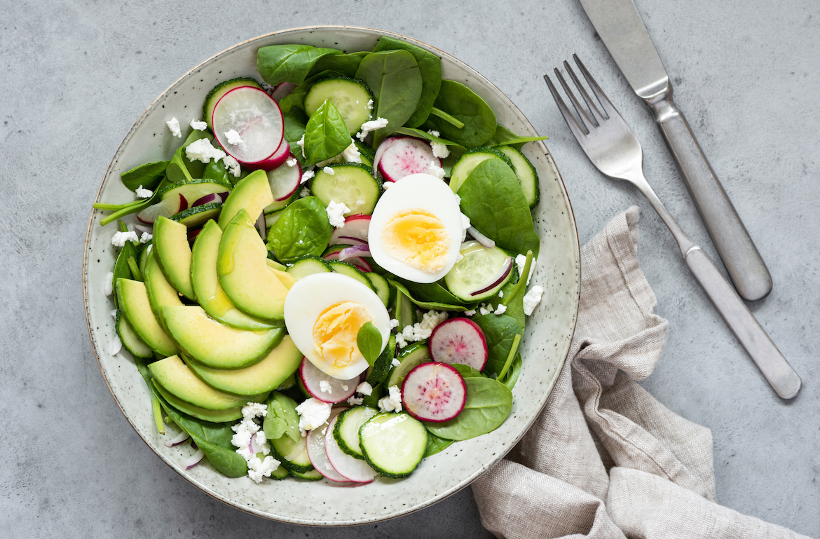 avocado for heart health spinach salad in bowl with hard boiled egg, radish, and avocado slices
