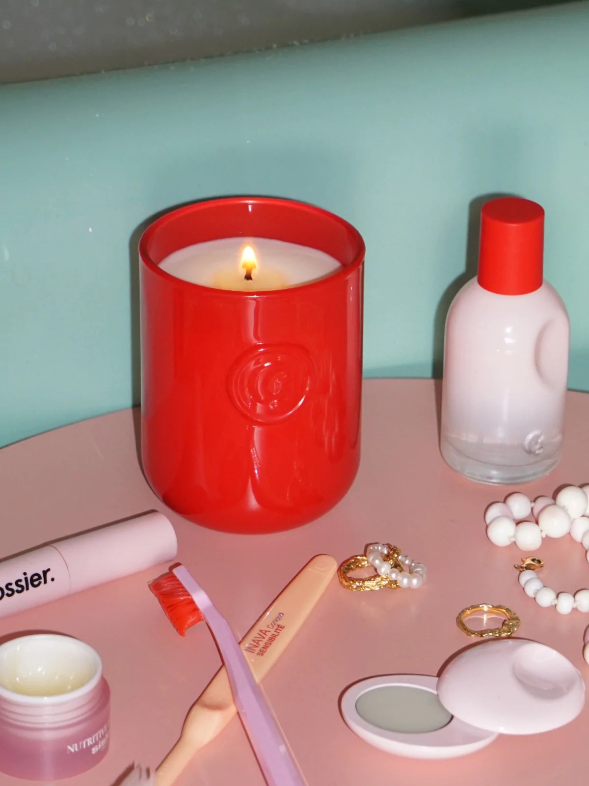 glossier you candle next to the perfume bottle on a table top