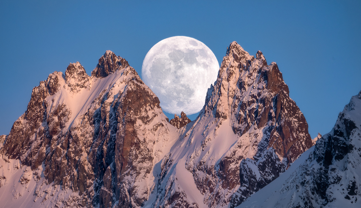 A full moon rises behind a snow-capped mountain, symbolizing full moon dreams.