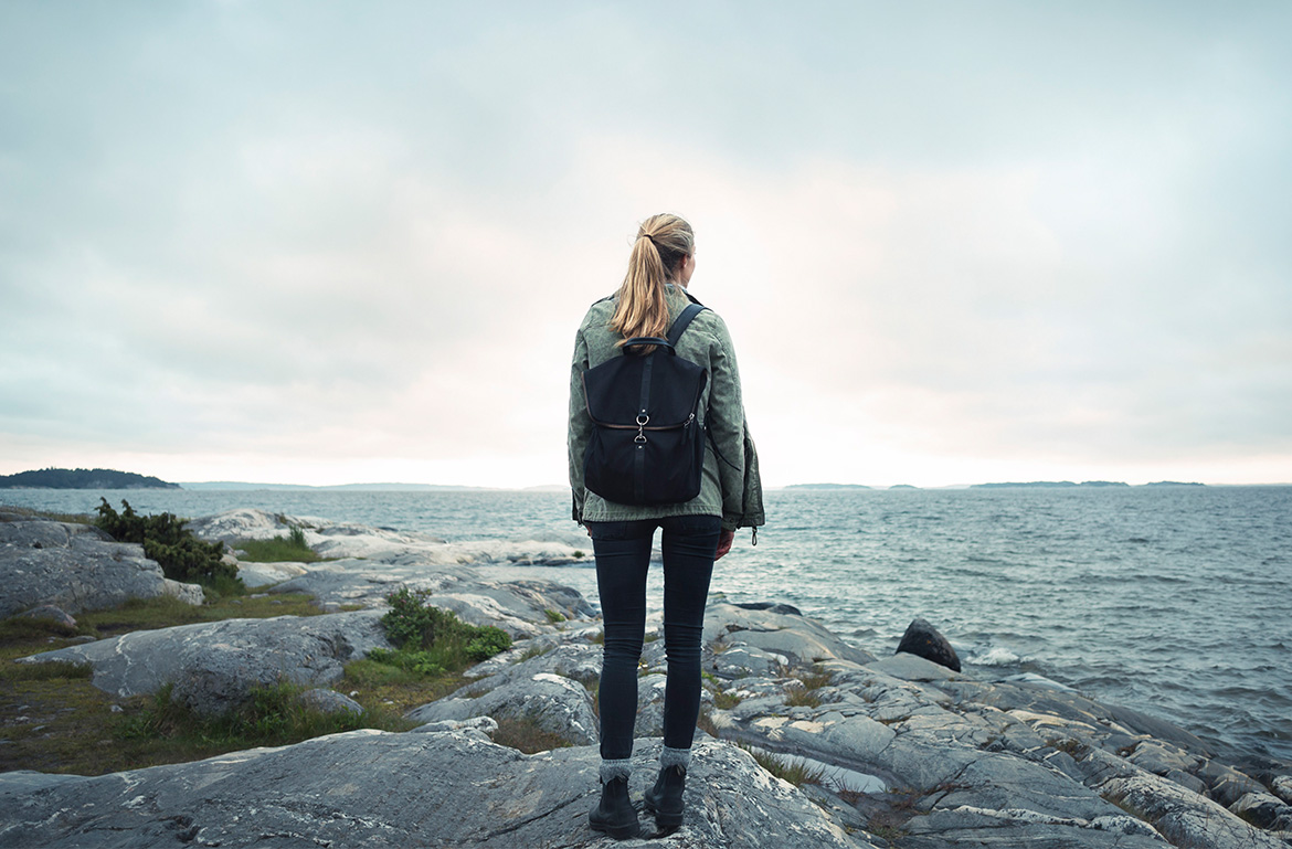 A woman wearing a backpack looks at the ocean.