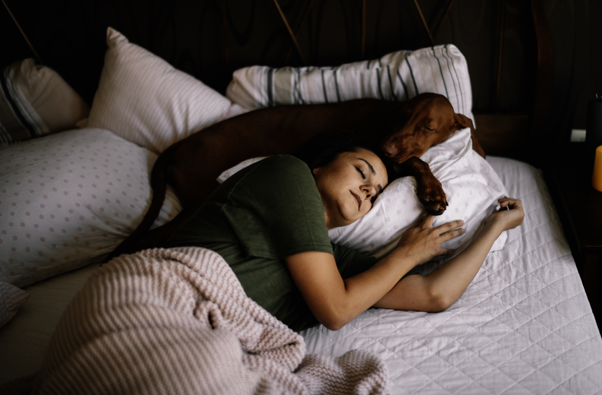 A woman sleeping on her side on a tmj pillow with a dog sleeping beside her