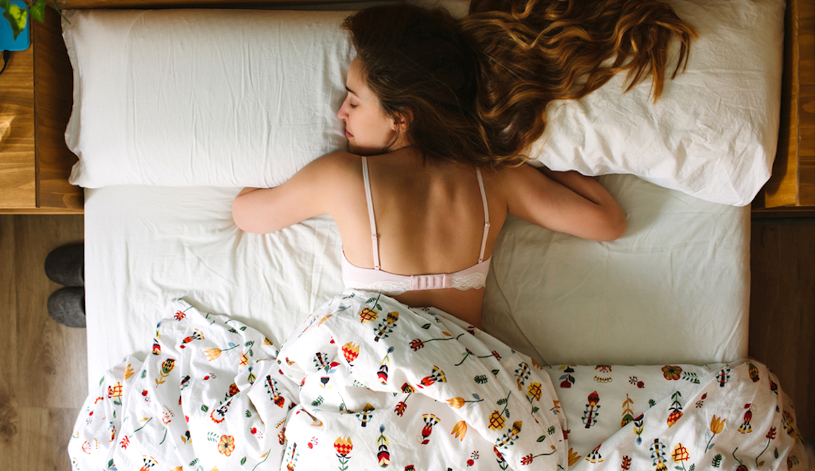 A woman sleeps on her stomach in bed, symbolizing the worst and best sleeping positions.