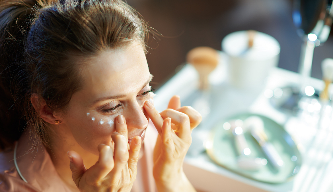 A mature woman applies under eye cream.