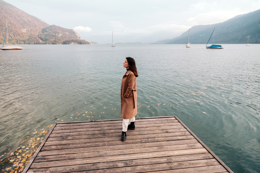 A woman wearing a coat stands on a dock near water.