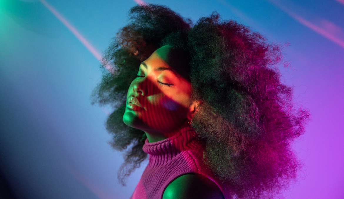A beautiful black woman stands with her eyes closed surrounded by neon colors, symbolizing lucid dream techniques.