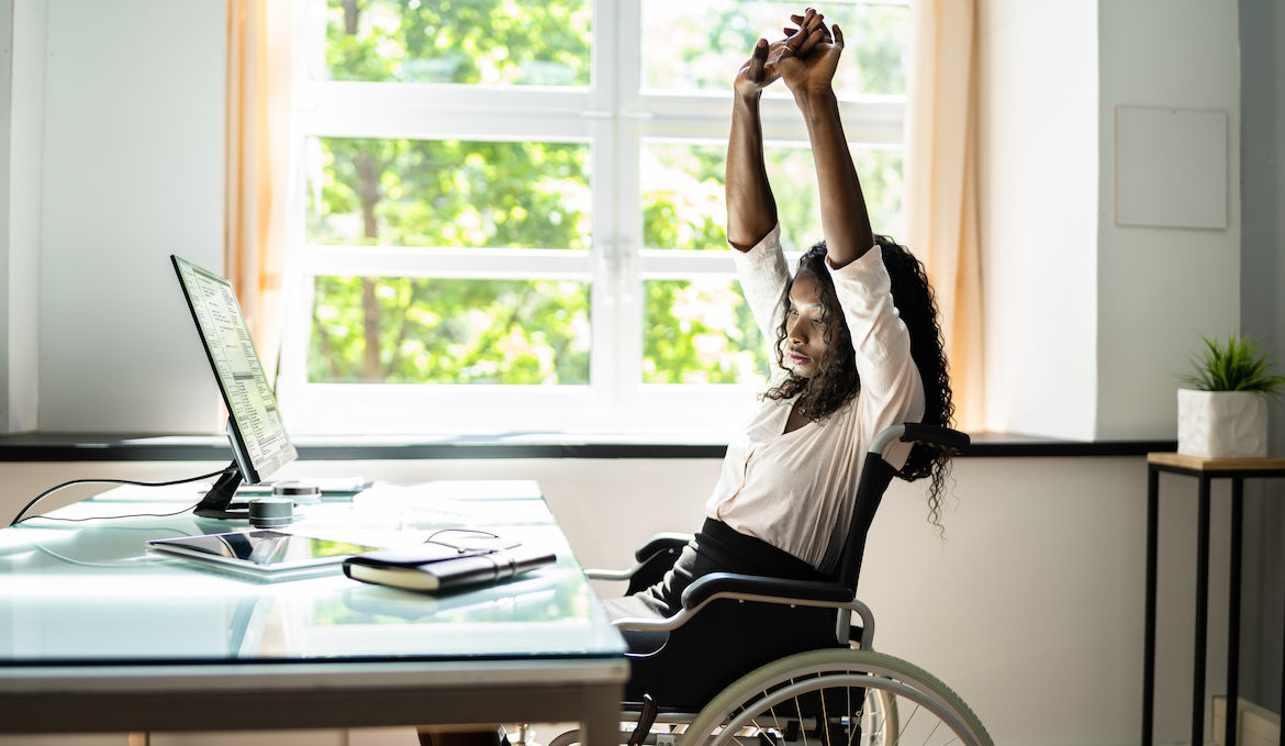 woman in wheelchair stretching at desk