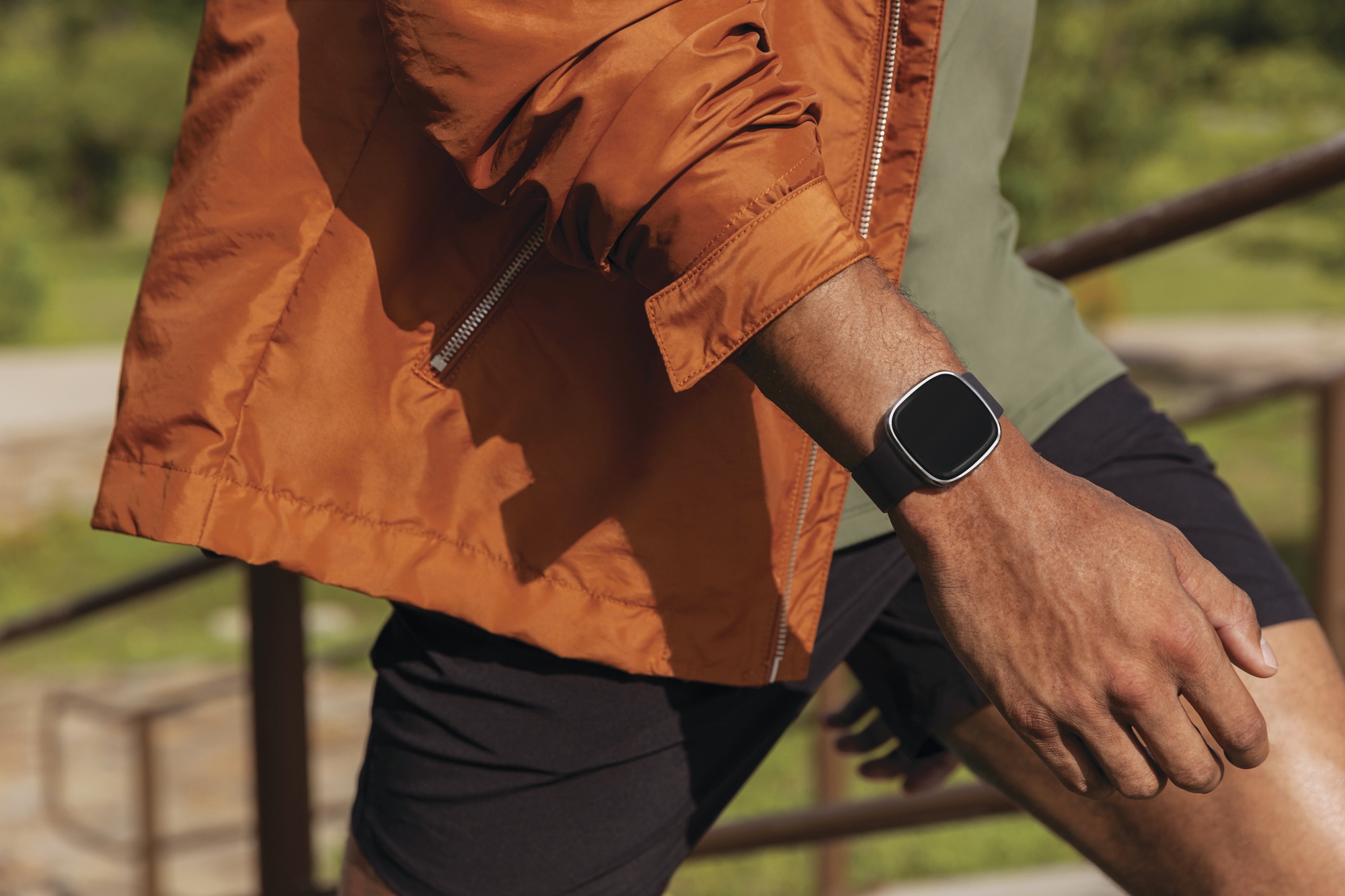 Man wearing Fitbit Sense fitness tracker, orange jacket, orange shirt, man's arm