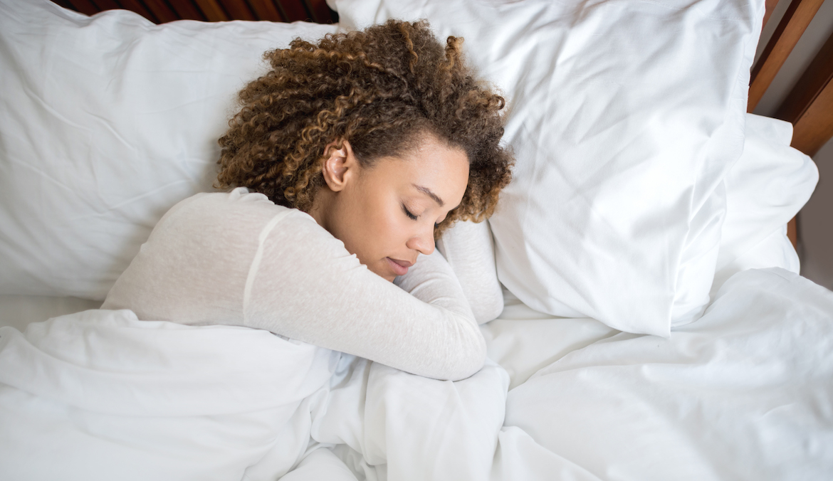 woman with curly hair sleeping in a white bed on her side