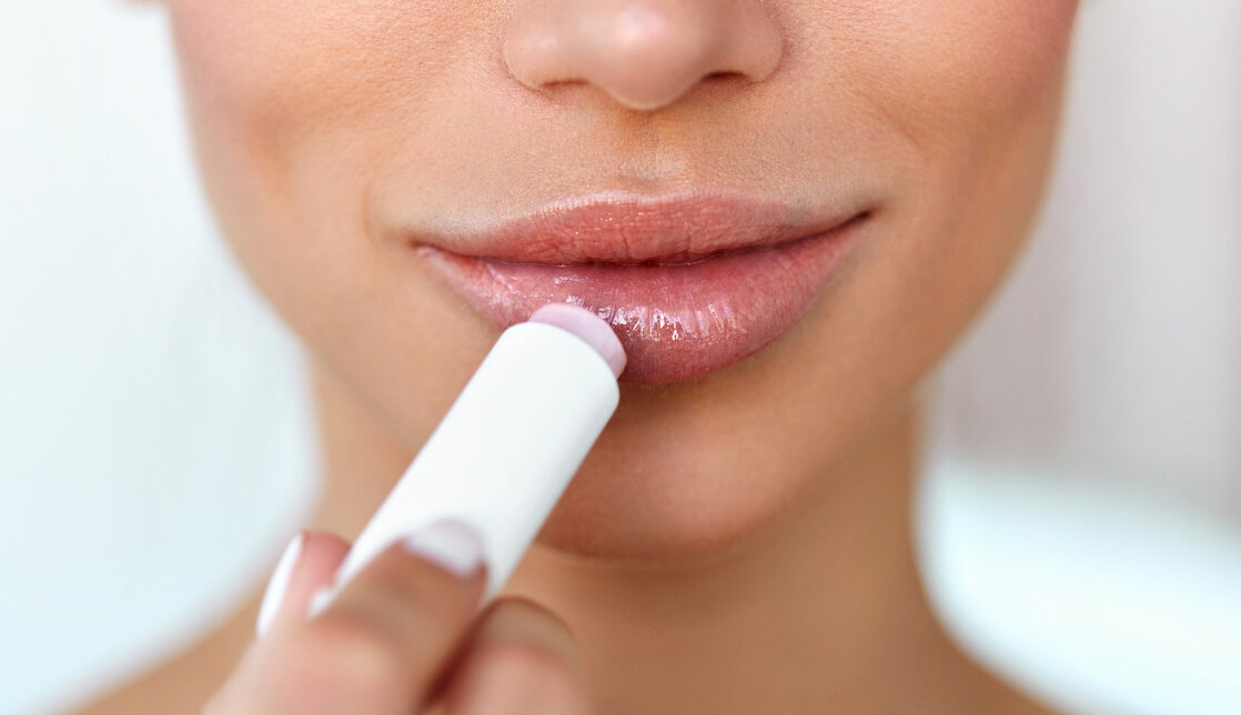 A woman applies a lip balm to her lips.