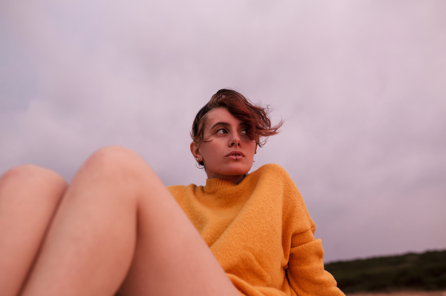 Young woman dressed in a yellow sweater looking pensive.