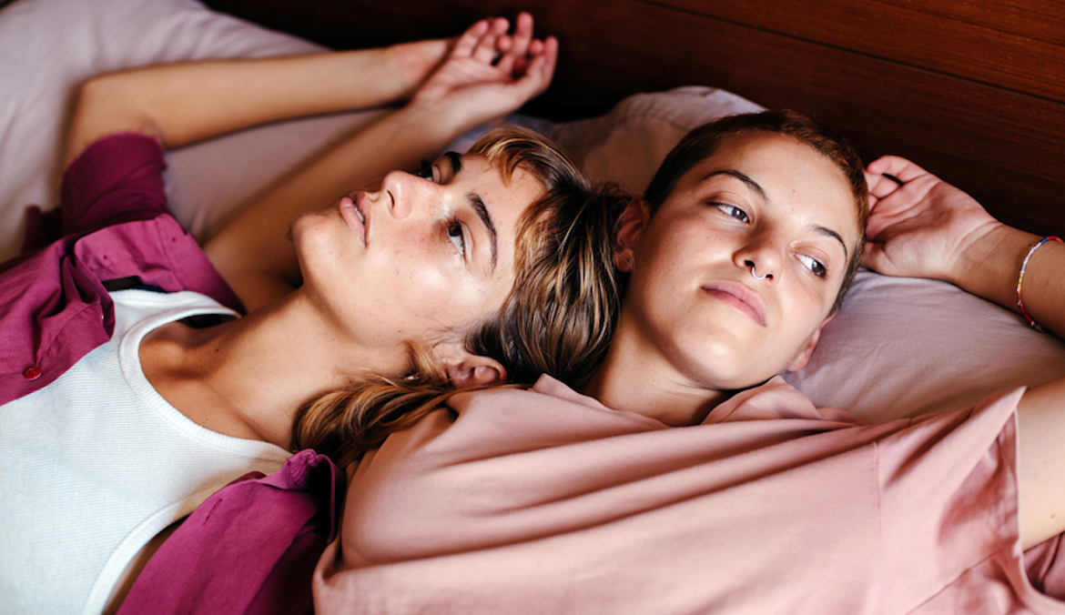 young lesbian couple lying in bed, looking thoughtful