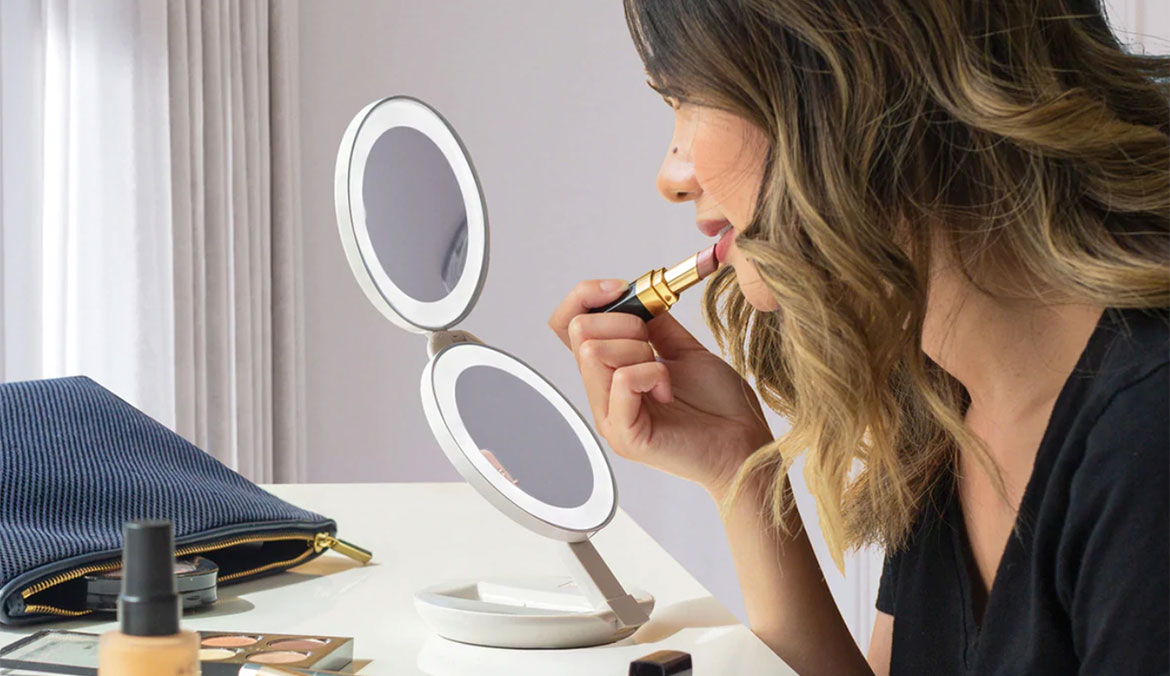 A woman applies lipstick while using a Zadro travel mirror.