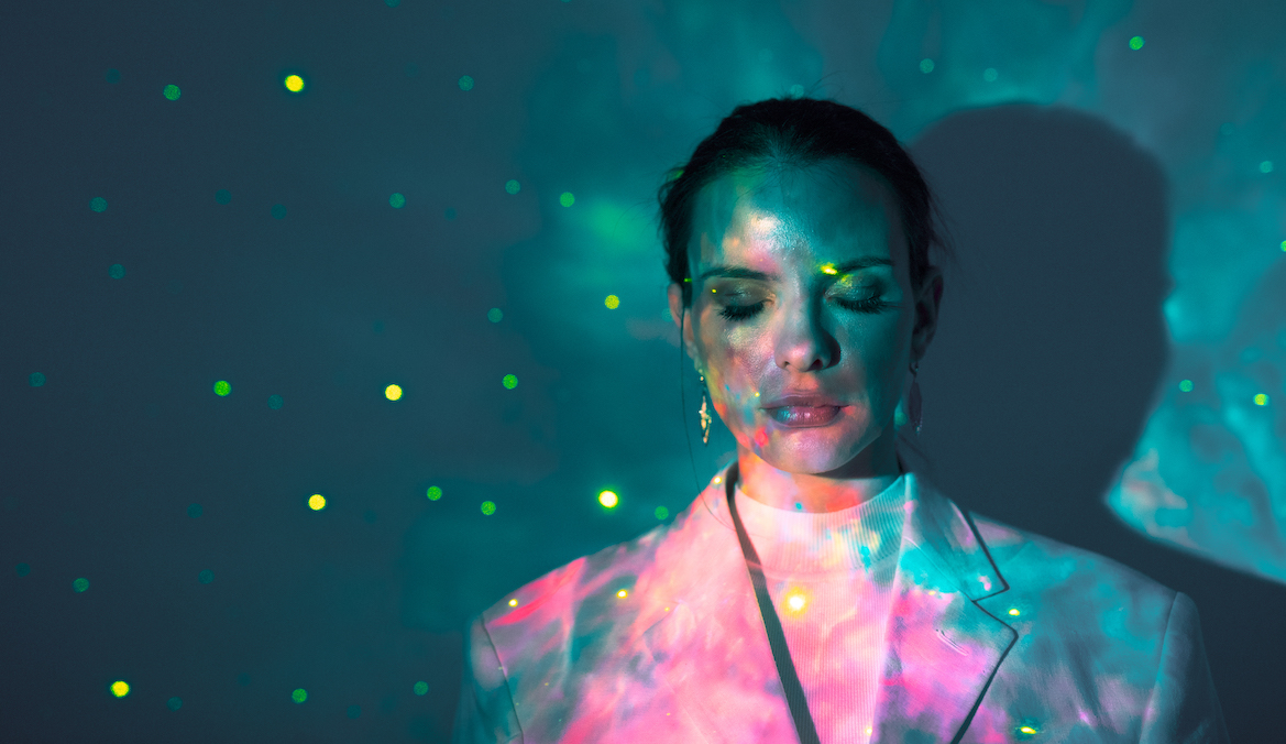 A multicolored light reflects onto a woman with eyes closed.