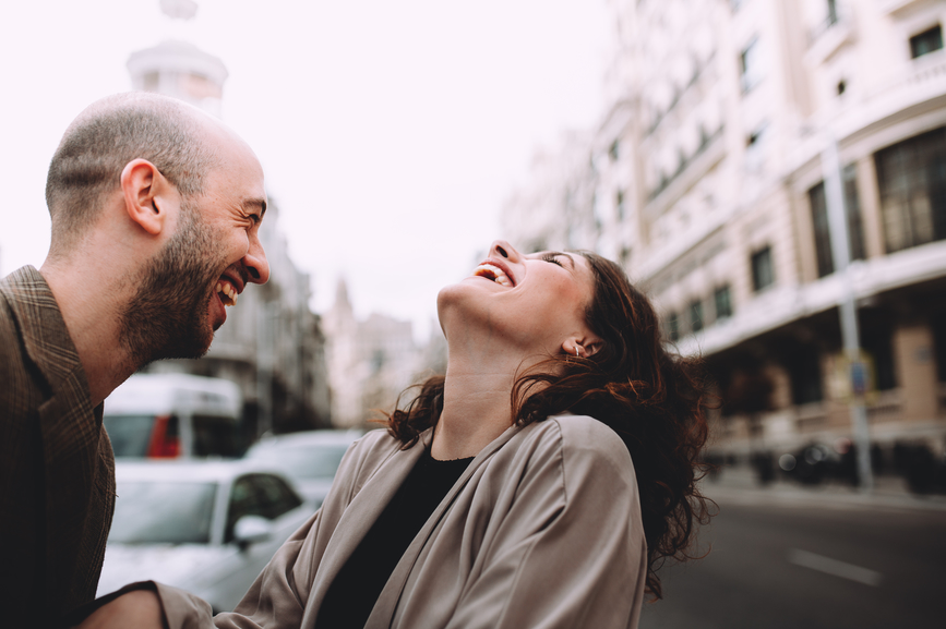 An attractive couple laughing in the street on a cloudy day in the city.
