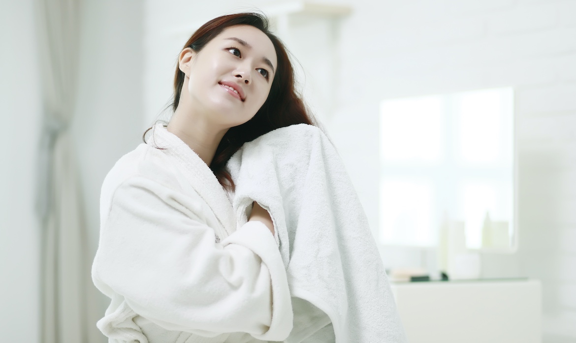 A woman dries her hair with a white towel.