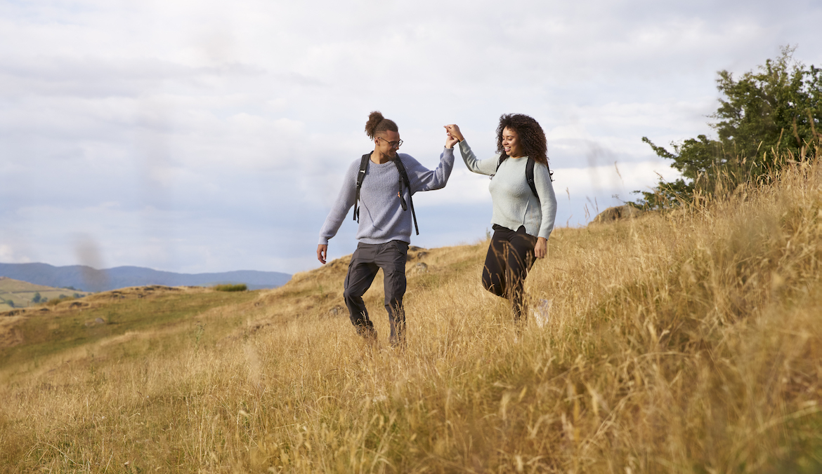 A man and a woman walking downhill through a field holding hands.