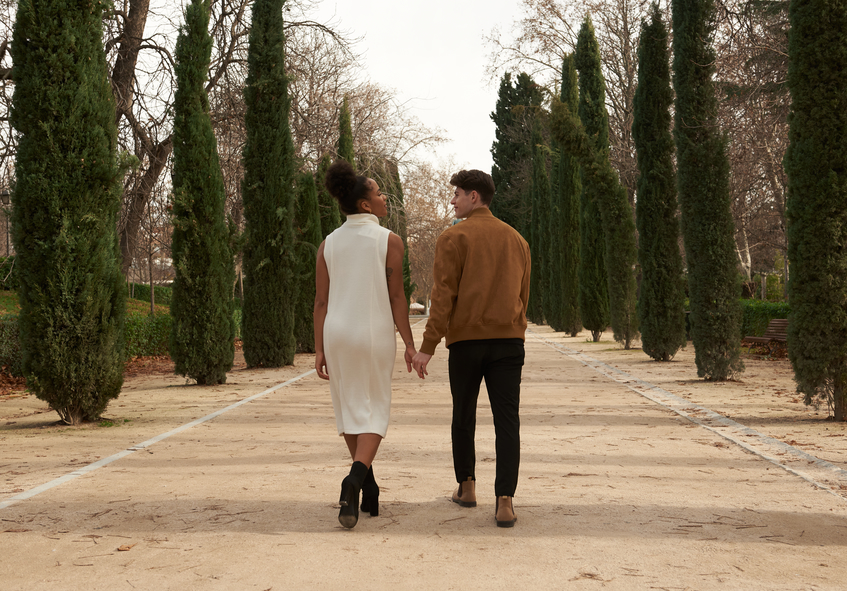 a couple walks hand in hand through a tree-lined pathway