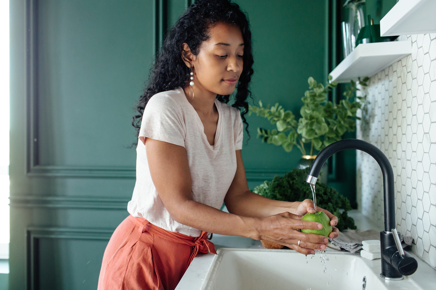 A woman at the sinks shows how to wash produce.