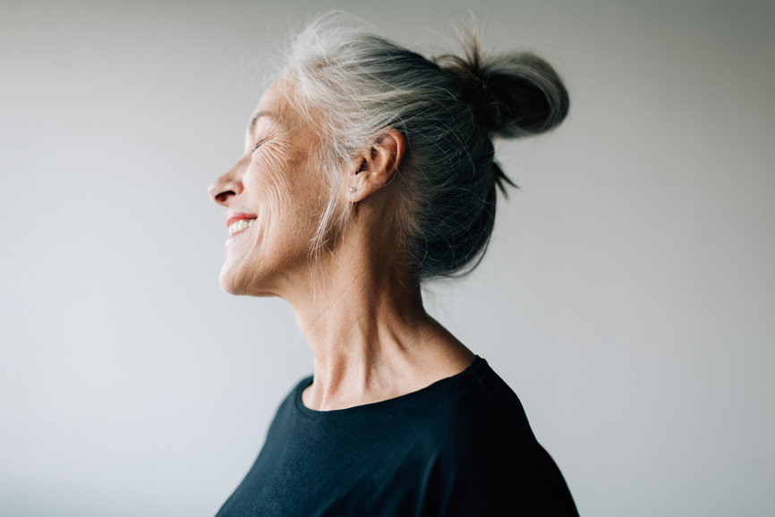 An older woman is smiling with her eyes closed, showing her jawline treated with Botox for TMJ.
