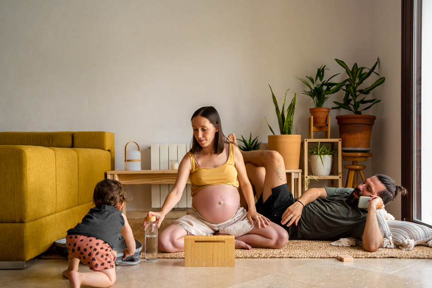 Prenatal parents and children sitting on the floor relaxing and using electronics at living room